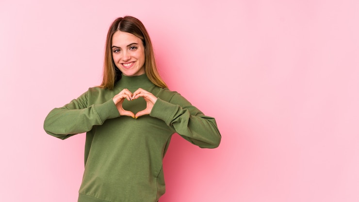 Foto mujer caucásica joven aislada en rosa que sonríe y que muestra una forma del corazón con las manos.