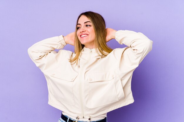 Mujer caucásica joven aislada en la sensación púrpura confidont, con las manos detrás de la cabeza.