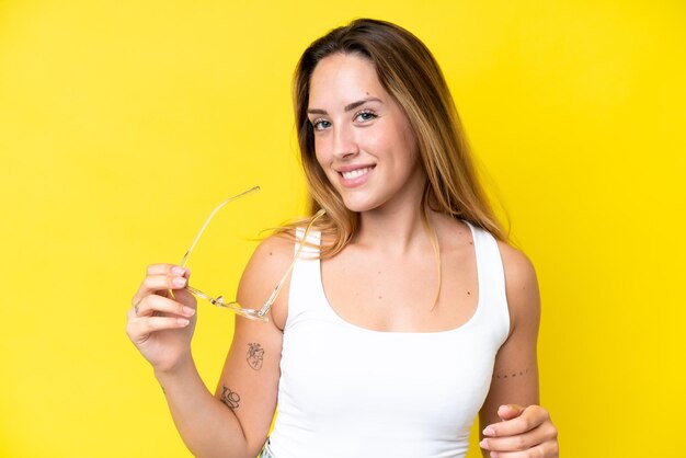 Mujer caucásica joven aislada sobre fondo amarillo con gafas con expresión feliz