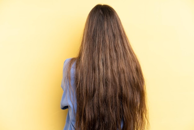 Mujer caucásica joven aislada sobre fondo amarillo en posición trasera