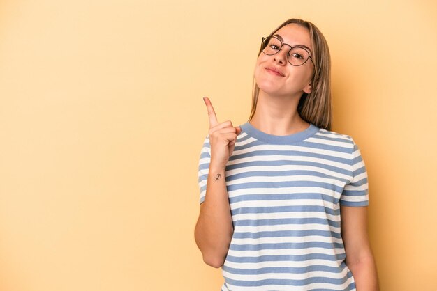 Mujer caucásica joven aislada sobre fondo amarillo que muestra el número uno con el dedo.