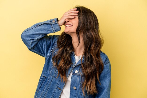 Mujer caucásica joven aislada sobre fondo amarillo se ríe alegremente manteniendo las manos en la cabeza Concepto de felicidad