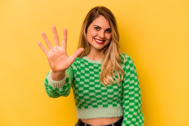 Mujer caucásica joven aislada sobre fondo amarillo sonriendo alegre mostrando el número cinco con los dedos