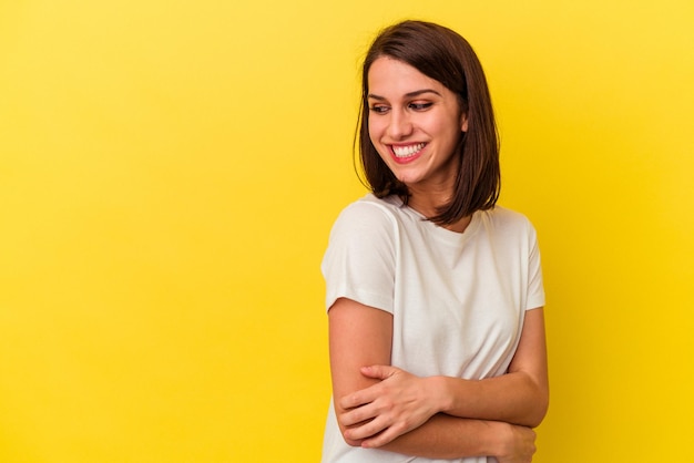 Mujer caucásica joven aislada sobre fondo amarillo sonriendo confiada con los brazos cruzados