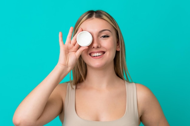 Mujer caucásica joven aislada sobre fondo azul con crema hidratante y felicidad