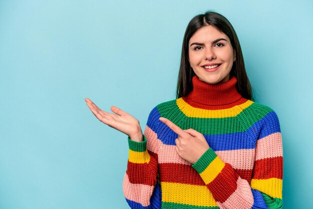 Mujer caucásica joven aislada sobre fondo azul emocionada sosteniendo un espacio de copia en la palma