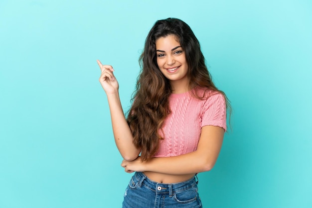 Mujer caucásica joven aislada sobre fondo azul feliz y apuntando hacia arriba