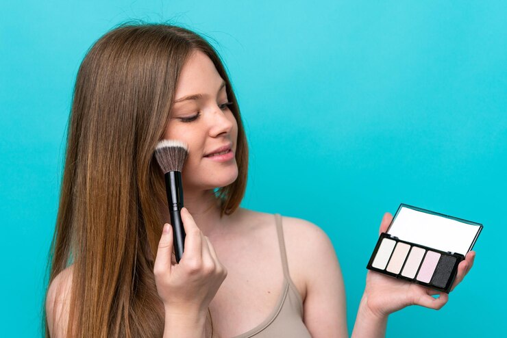 Foto mujer caucásica joven aislada sobre fondo azul con paleta de maquillaje y feliz