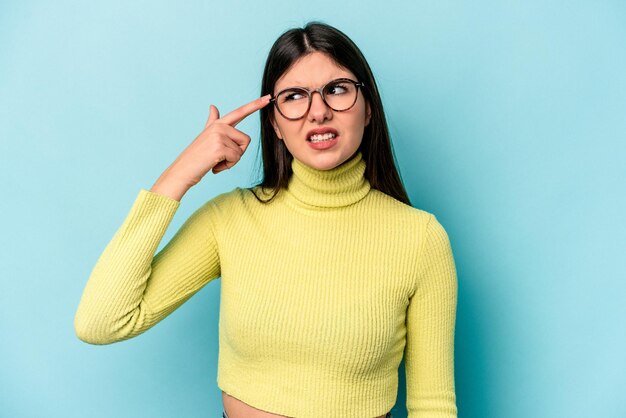 Mujer caucásica joven aislada sobre fondo azul que cubre las orejas con las manos