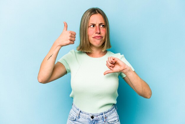 Mujer caucásica joven aislada sobre fondo azul que muestra los pulgares hacia arriba y hacia abajo es difícil elegir el concepto