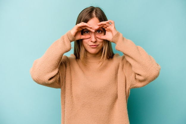 Mujer caucásica joven aislada sobre fondo azul que muestra un signo bien sobre los ojos