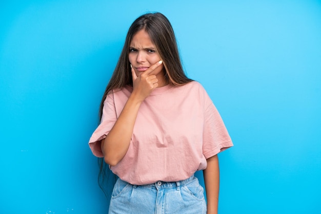 Mujer caucásica joven aislada sobre fondo azul que tiene dudas