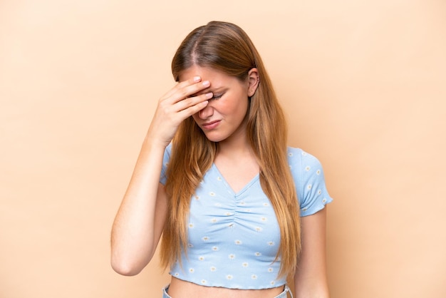 Mujer caucásica joven aislada sobre fondo beige con dolor de cabeza