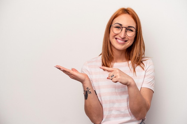 Mujer caucásica joven aislada sobre fondo blanco emocionada sosteniendo un espacio de copia en la palma.