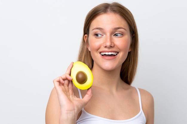 Mujer caucásica joven aislada sobre fondo blanco sosteniendo un aguacate mientras sonríe Retrato de primer plano