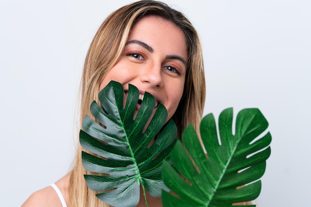 Mujer caucásica joven aislada sobre fondo blanco sosteniendo una hoja de palma con expresión feliz Retrato de primer plano