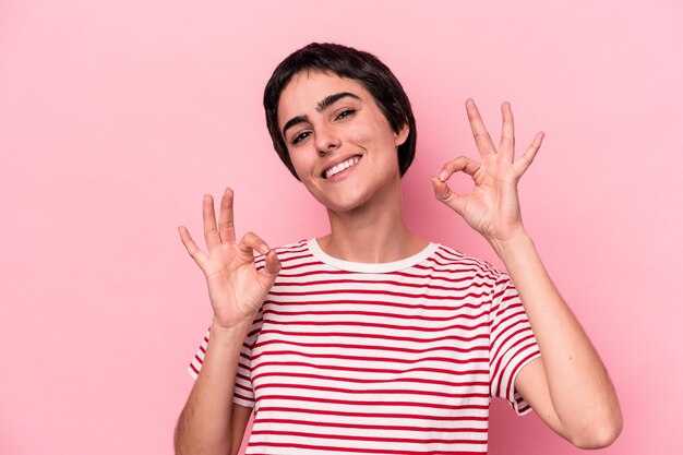 Mujer caucásica joven aislada sobre fondo rosa alegre y confiada mostrando gesto ok