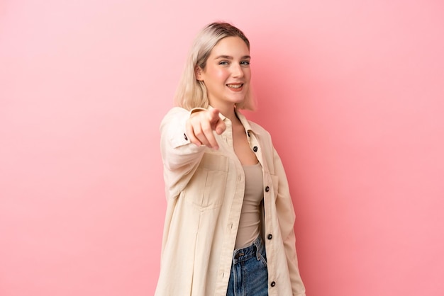 Mujer caucásica joven aislada sobre fondo rosa apuntando al frente con expresión feliz