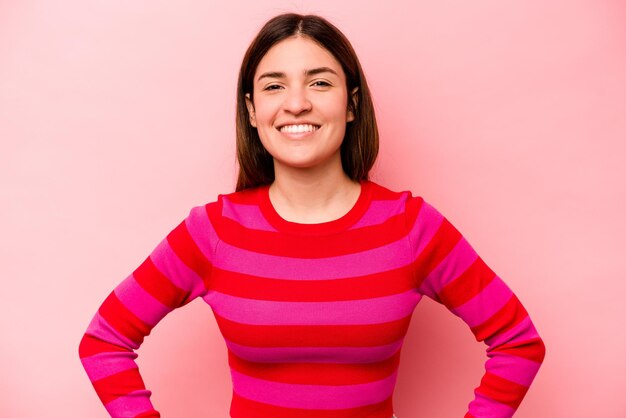 Mujer caucásica joven aislada sobre fondo rosa confiada manteniendo las manos en las caderas