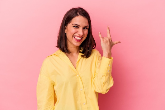 Mujer caucásica joven aislada sobre fondo rosa mostrando gesto de roca con los dedos