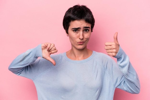 Mujer caucásica joven aislada sobre fondo rosa que muestra los pulgares hacia arriba y hacia abajo es difícil elegir el concepto