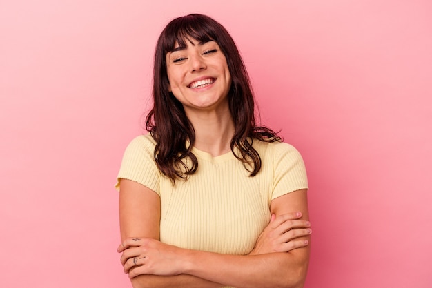 Mujer caucásica joven aislada sobre fondo rosa que se siente segura, cruzando los brazos con determinación.