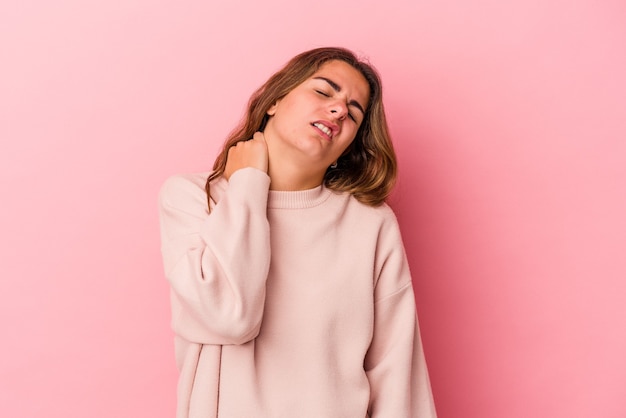 Mujer caucásica joven aislada sobre fondo rosa que sufre dolor de cuello debido al estilo de vida sedentario.