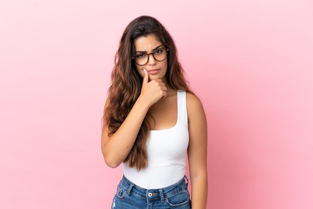 Mujer caucásica joven aislada sobre fondo rosa que tiene dudas