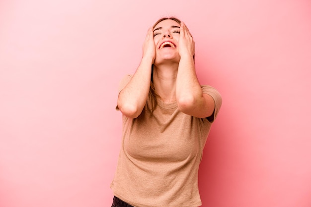 Mujer caucásica joven aislada sobre fondo rosa se ríe alegremente manteniendo las manos en la cabeza Concepto de felicidad