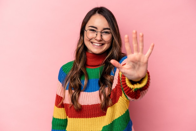 Mujer caucásica joven aislada sobre fondo rosa sonriendo alegre mostrando el número cinco con los dedos