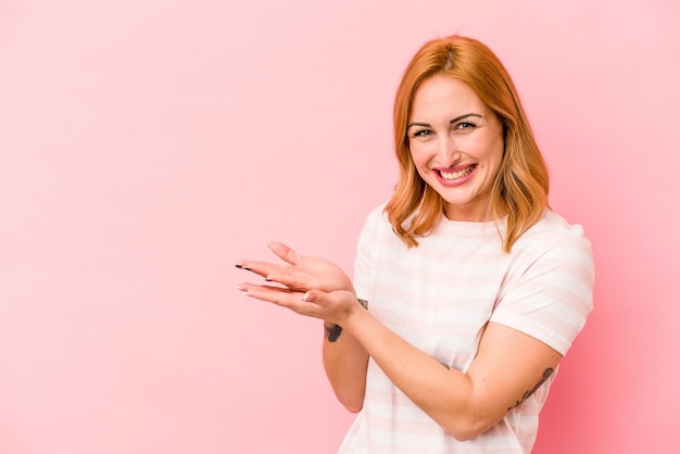 Mujer caucásica joven aislada sobre fondo rosa sosteniendo un espacio de copia en una palma.