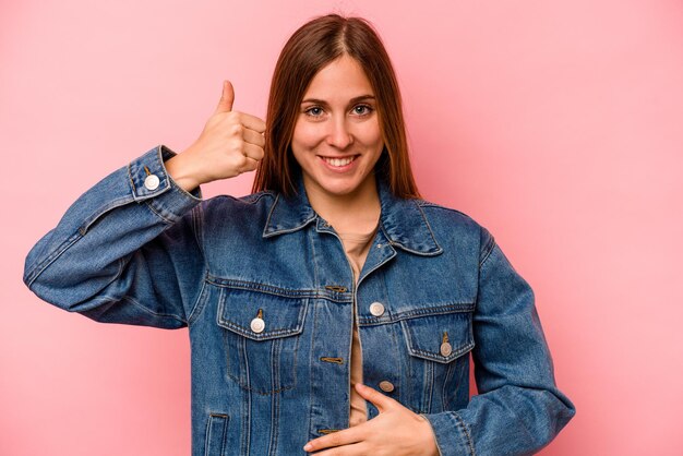 Mujer caucásica joven aislada sobre fondo rosa toca sonrisas de barriga comiendo suavemente y concepto de satisfacción