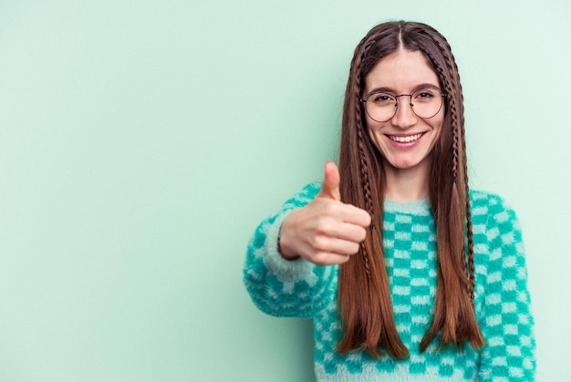 Mujer caucásica joven aislada sobre fondo verde sonriendo y levantando el pulgar