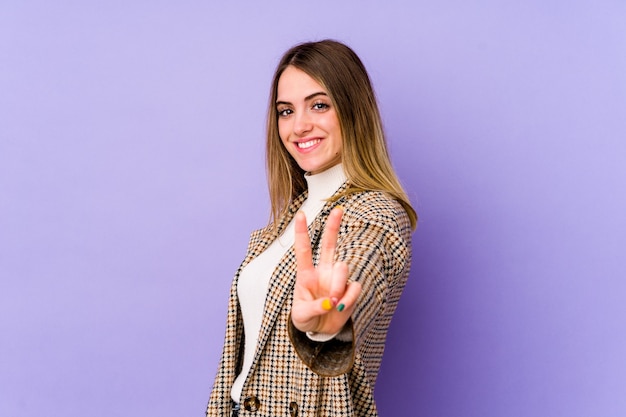 Mujer caucásica joven aislada sobre púrpura mostrando el signo de la victoria y sonriendo ampliamente.