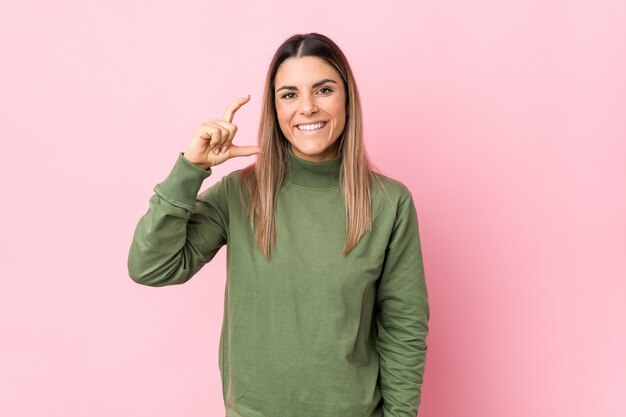 Mujer caucásica joven aislada sosteniendo algo poco con los dedos índices, sonriente y confiado.