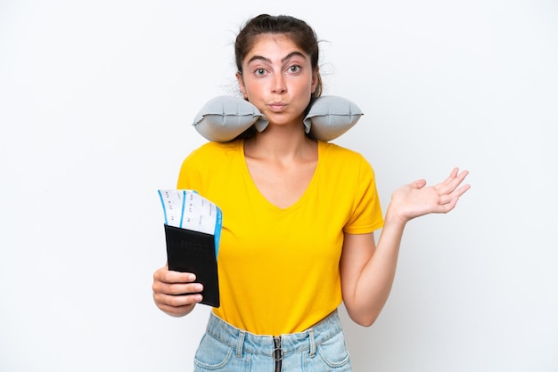 Mujer caucásica joven con almohada de viaje inflable aislada de fondo blanco que tiene dudas mientras levanta las manos