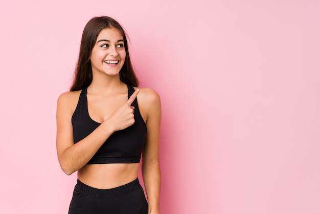 La mujer caucásica joven de la aptitud que hacía deporte aisló sonriendo y señalando a un lado, mostrando algo en el espacio en blanco.