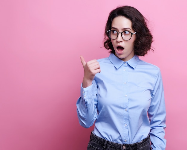 La mujer caucásica joven apuesto en gafas transparentes redondas, mantiene la mano levantada, vestida con ropa informal,