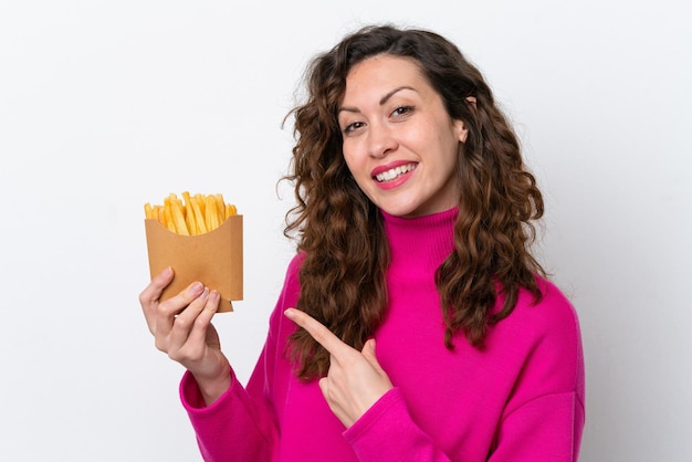 Mujer caucásica joven atrapando papas fritas aisladas de fondo blanco y apuntándolas