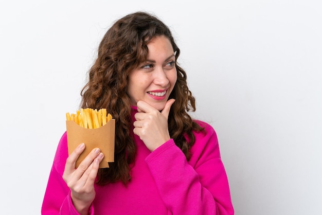 Mujer caucásica joven atrapando papas fritas aisladas en fondo blanco pensando en una idea y mirando hacia un lado