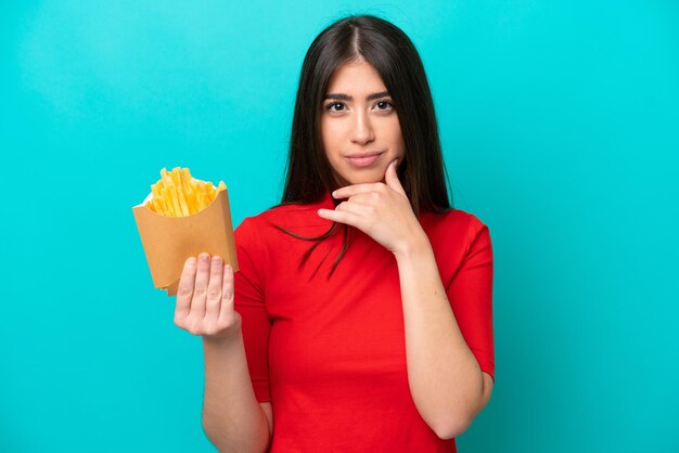 Mujer caucásica joven atrapando papas fritas aisladas en el pensamiento de fondo azul