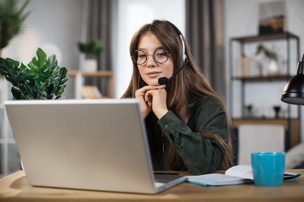 Mujer caucásica joven con auriculares hablando durante el chat de video en una computadora portátil moderna