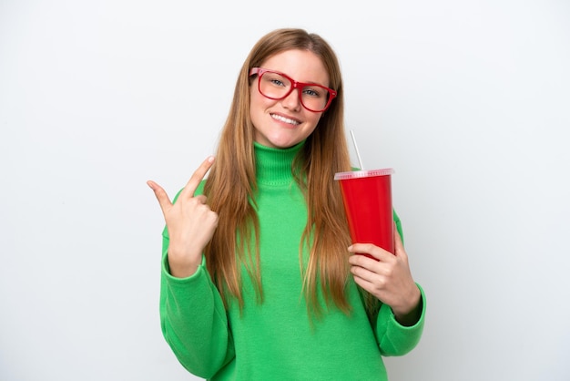 Mujer caucásica joven bebiendo refresco aislado sobre fondo blanco dando un gesto de aprobación