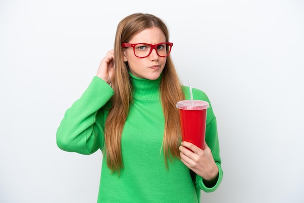 Mujer caucásica joven bebiendo refresco aislado sobre fondo blanco que tiene dudas