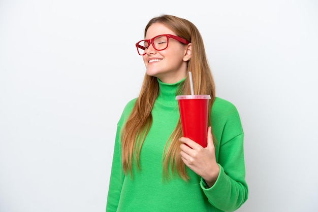 Mujer caucásica joven bebiendo refresco aislado sobre fondo blanco riendo en posición lateral