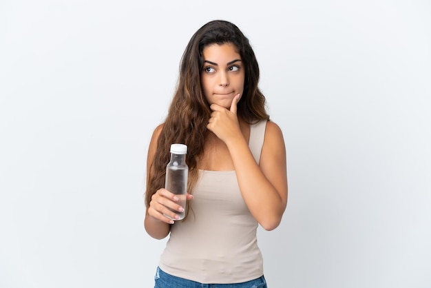 Mujer caucásica joven con una botella de agua aislada en el fondo blanco que tiene dudas y pensamiento