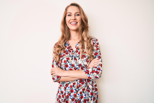 Mujer caucásica joven con cabello rubio con vestido de verano cara feliz sonriendo con los brazos cruzados mirando a la persona positiva de la cámara