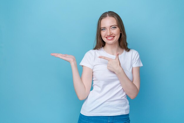 Mujer caucásica joven en camiseta blanca y jeans sonriendo alegremente señalando