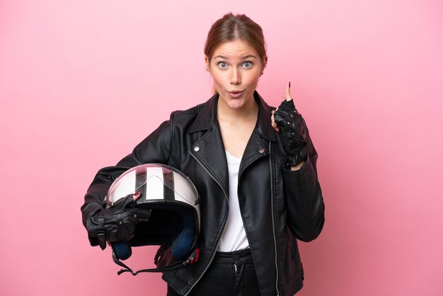 Mujer caucásica joven con un casco de motocicleta aislado en un fondo rosado con la intención de darse cuenta de la solución mientras levanta un dedo