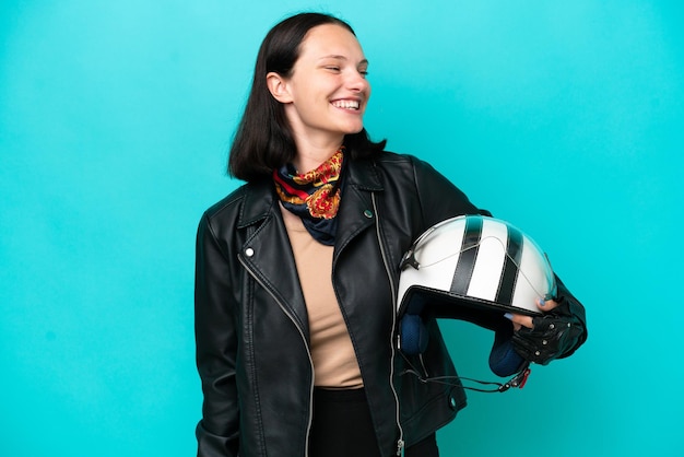 Foto mujer caucásica joven con un casco de motocicleta aislado sobre fondo azul mirando hacia el lado